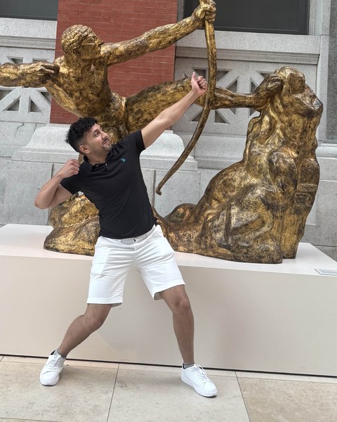Ryan Raghubans mirroring the pose of a gilded archer statue in a museum courtyard.